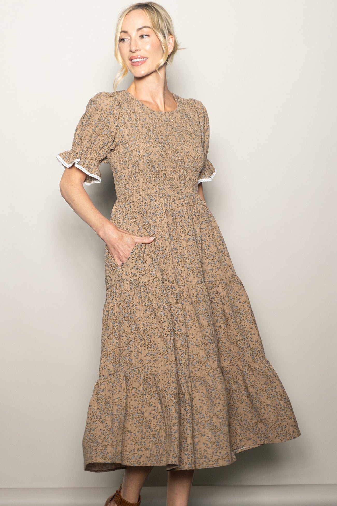woman wearing a brown floral midi dress with puff sleeves and pockets, standing against a neutral background