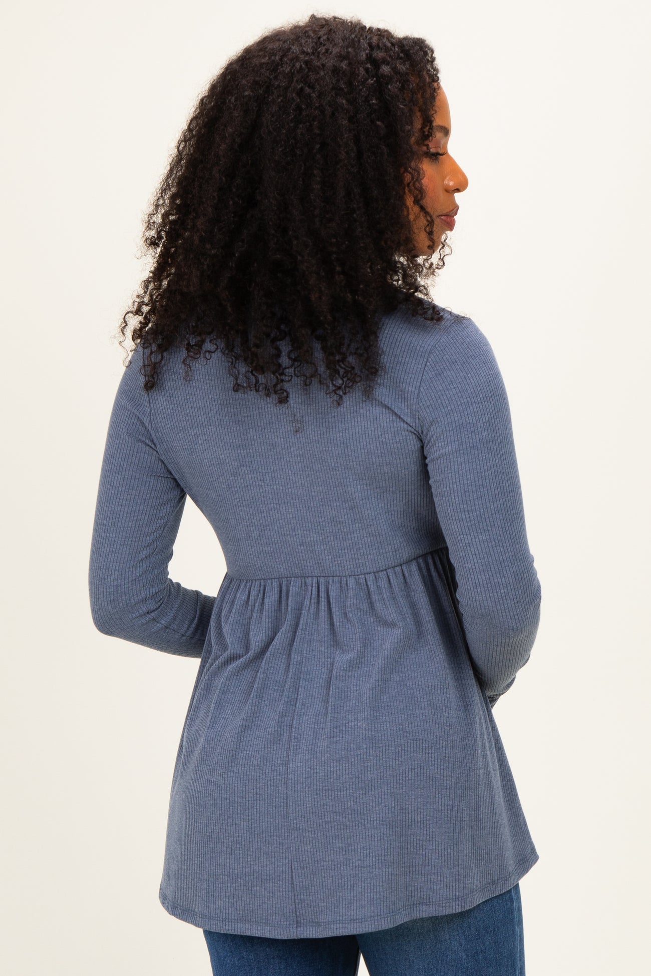 woman wearing a navy ribbed long sleeve top with a peplum hem and curly hair, shown from the back