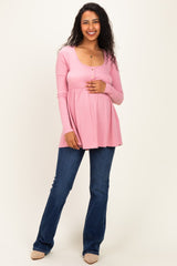 woman wearing a pink long sleeve maternity top with buttons and a baby bump, paired with blue flared jeans