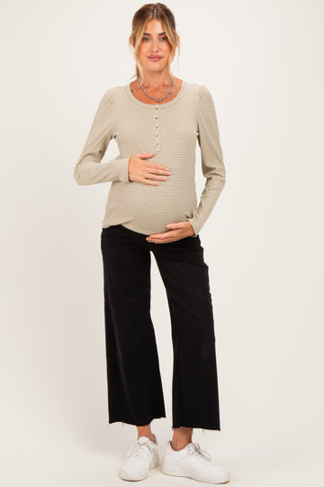 woman wearing a beige striped maternity top with button details and black wide-leg maternity pants, holding her baby bump