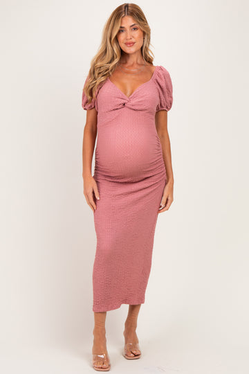 woman wearing a pink smocked maternity dress with puff sleeves and a twist detail, showcasing her baby bump