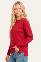 woman wearing a red long sleeve sweater with side slits and relaxed fit, paired with blue jeans