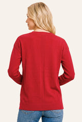 woman wearing a back view of a red long sleeve sweater with a relaxed fit and ribbed hem, paired with blue jeans