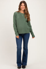 woman wearing a green maternity sweater and flared jeans, with a visible baby bump