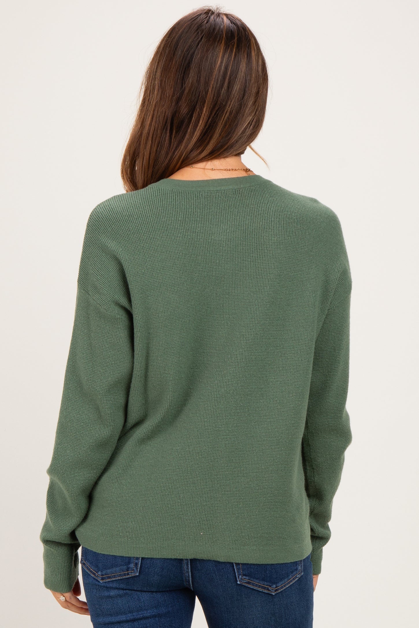 woman wearing a green long sleeve maternity sweater from the back with jeans