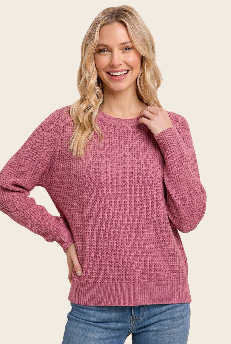 woman wearing a cozy pink knit sweater with long sleeves and a relaxed fit, smiling while posing