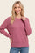 woman wearing a cozy pink knit sweater with long sleeves and a relaxed fit, smiling while posing