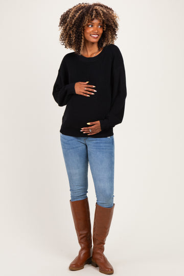 woman wearing a black maternity sweater and blue jeans, holding her baby bump and smiling