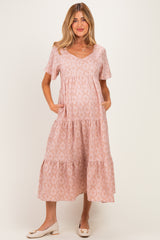 woman wearing a light pink maternity dress with a v-neck, short sleeves, and tiered skirt, holding her baby bump