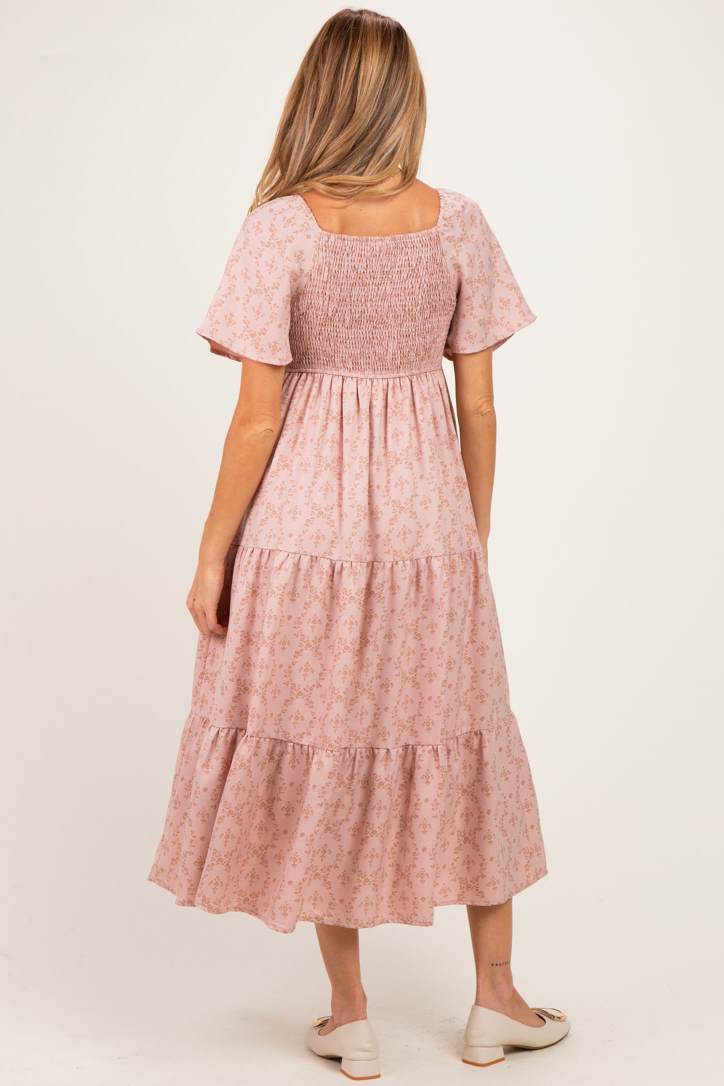 woman wearing a pink floral maternity dress with short sleeves and a smocked bodice, showing a baby bump