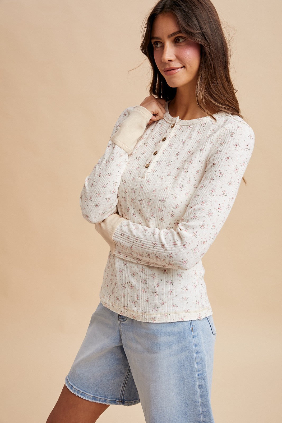 woman wearing a cream floral long sleeve henley top with buttons and light blue denim shorts
