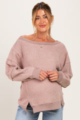 woman wearing a light pink oversized maternity sweater with boat neckline and ribbed texture, gently cradling her baby bump