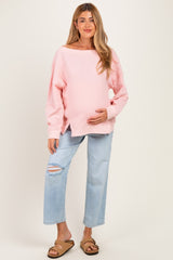 woman wearing a pink ribbed maternity sweater and holding her baby bump with light blue ripped jeans