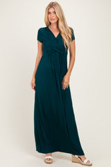 woman wearing a dark green short sleeve maxi dress with a twist front detail and standing in neutral sandals