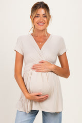 woman wearing a beige maternity top with short sleeves, holding her baby bump and smiling