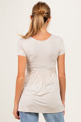 woman wearing a light beige short sleeve maternity top with a gathered waistline from the back