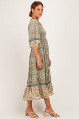 woman wearing a green floral midi dress with puff sleeves and a tiered hem, paired with beige slide sandals