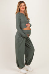 woman wearing a sage green long sleeve maternity top and matching pants, cradling her baby bump