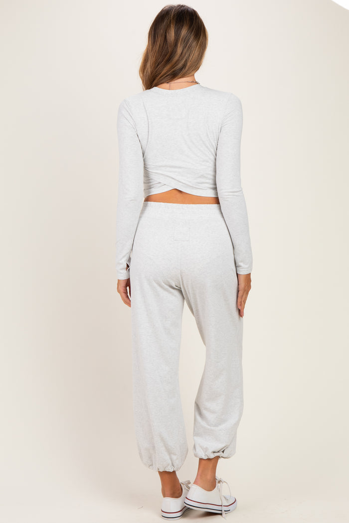 woman wearing a light gray maternity long sleeve crop top and matching jogger pants, showing a baby bump