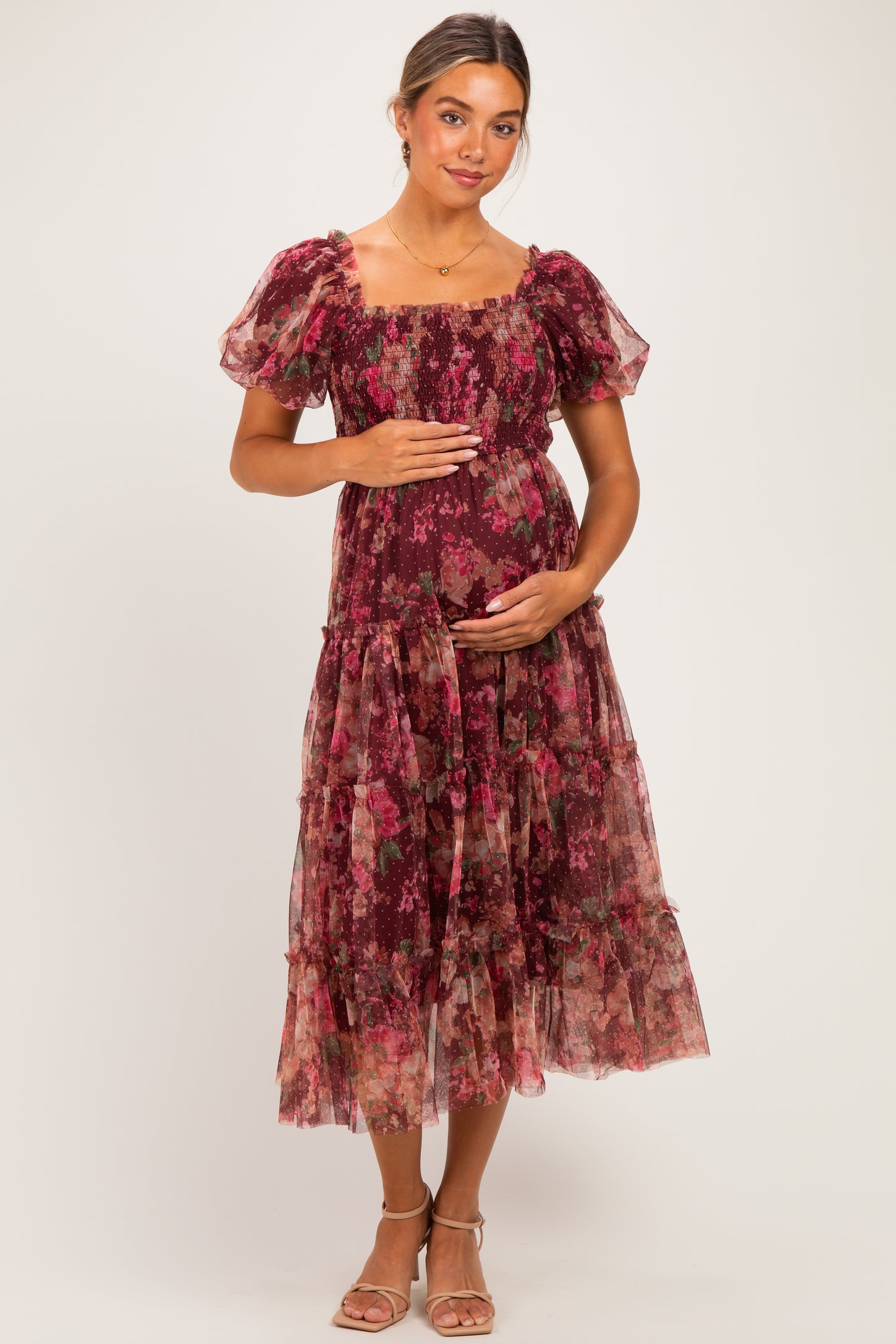 woman wearing a burgundy floral maternity dress with puff sleeves, holding her baby bump