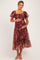 woman wearing a burgundy floral maternity dress with puff sleeves, holding her baby bump