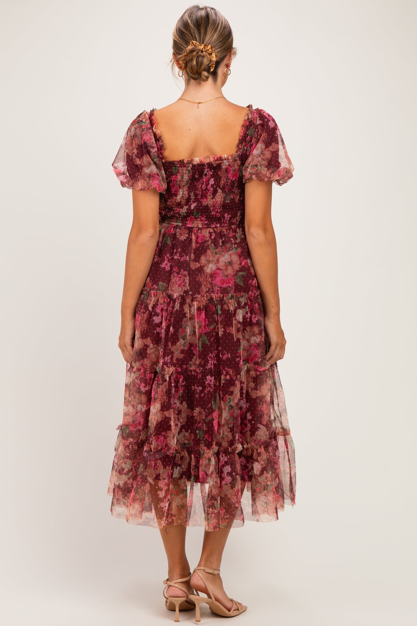 woman wearing a floral burgundy maternity dress with short puff sleeves and a tiered skirt, showing a baby bump from behind
