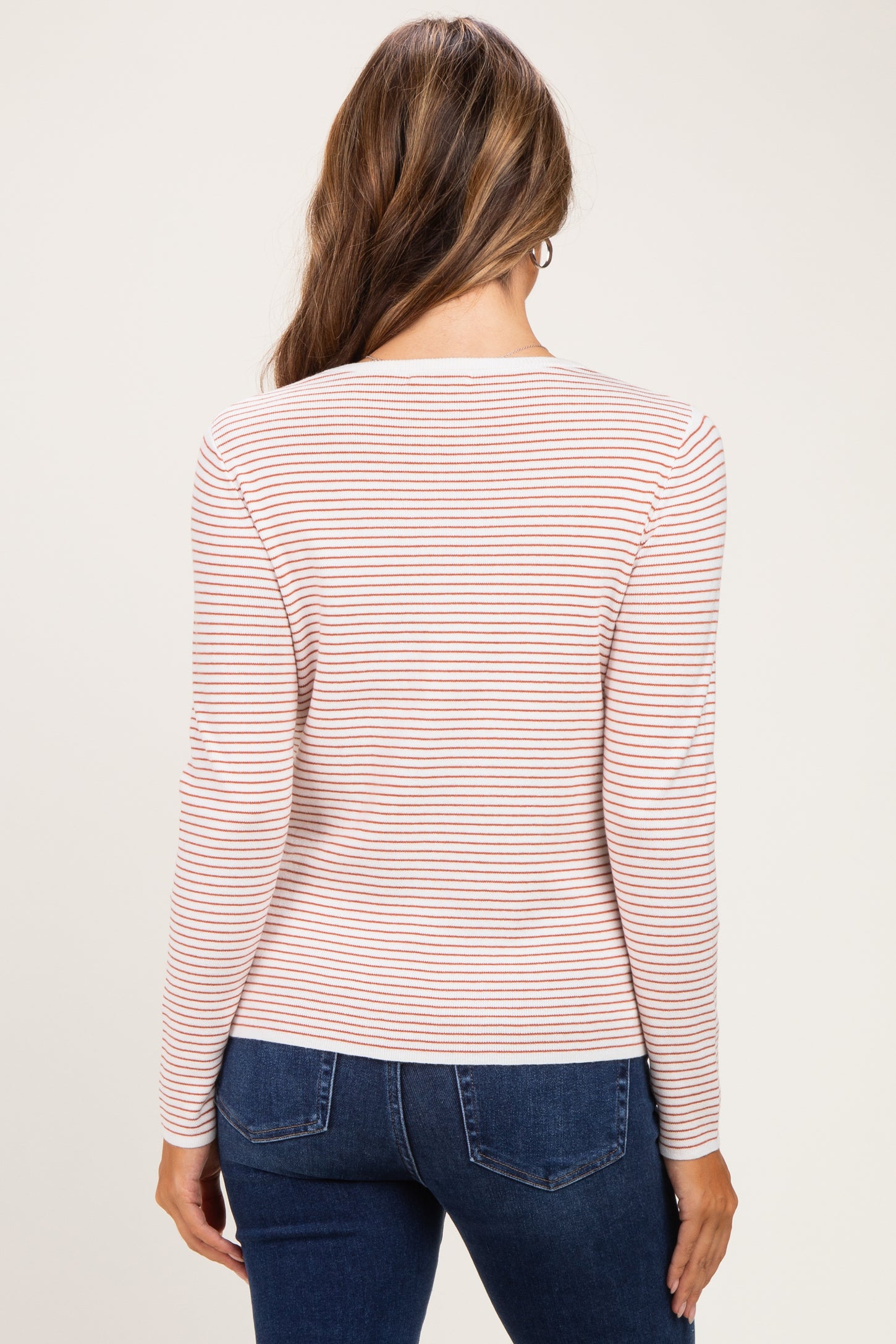 woman wearing a light pink and white striped long sleeve maternity top seen from the back, paired with denim jeans