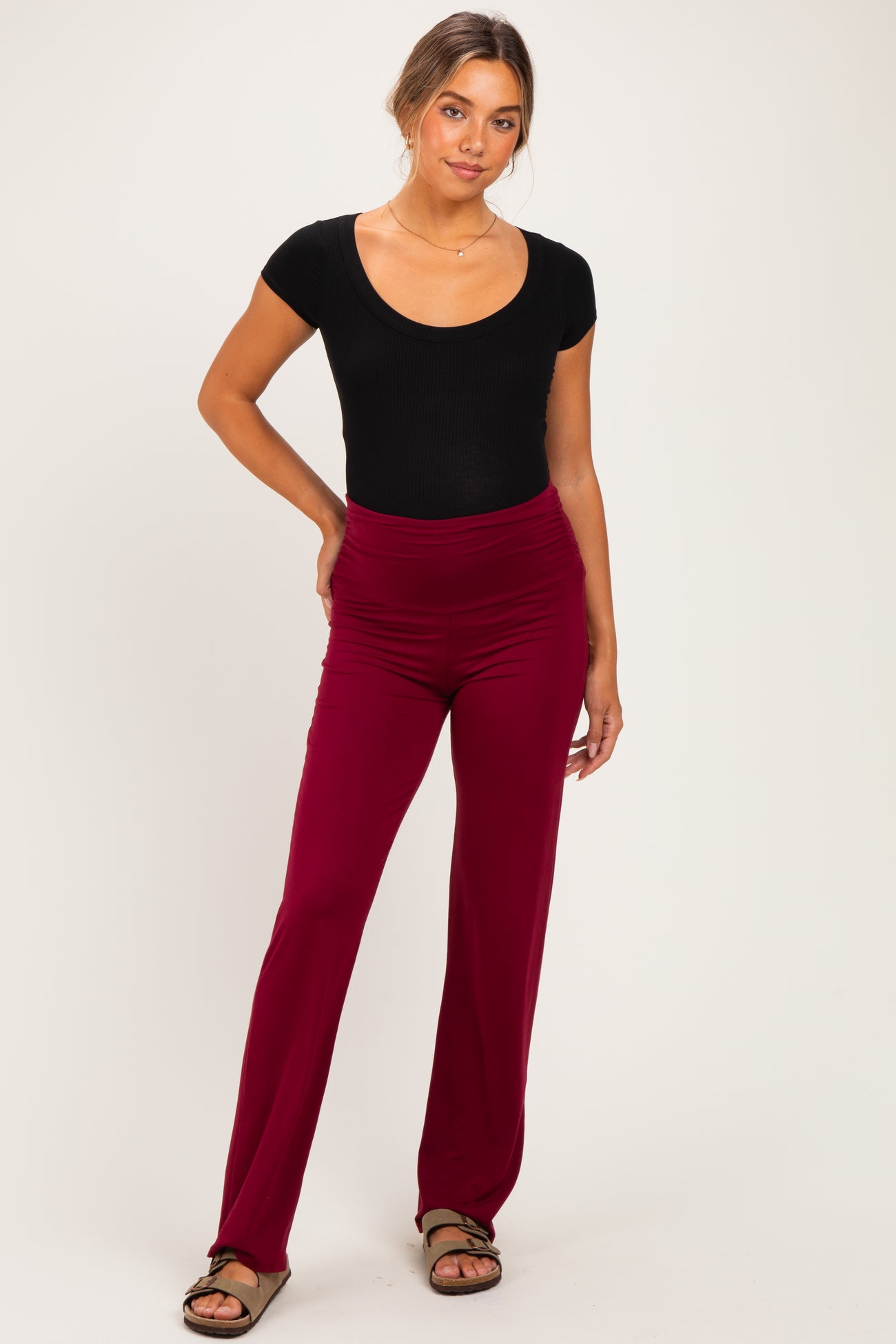 woman wearing a black scoop neck bodysuit and burgundy maternity pants with a ruched waistband