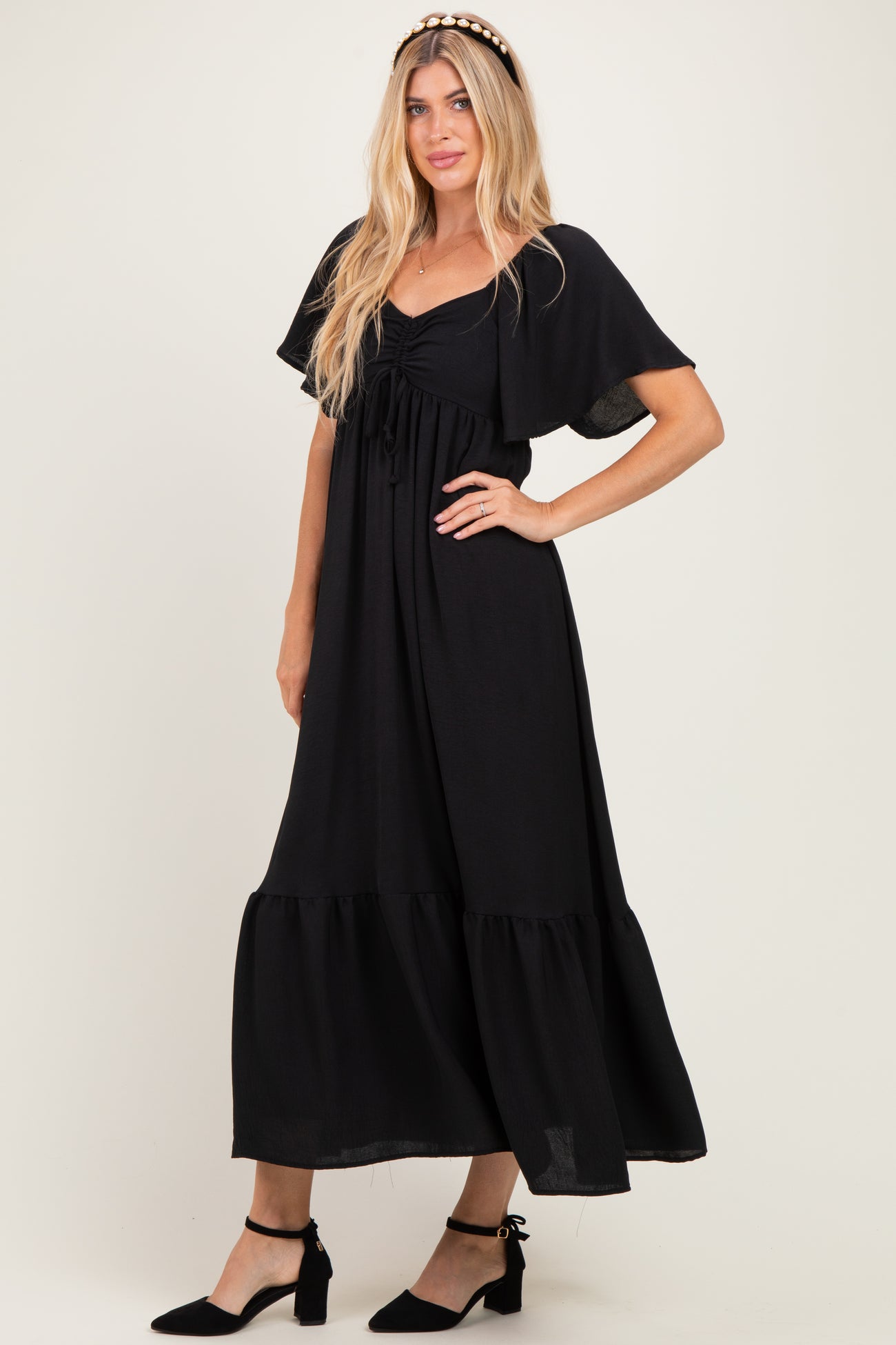 woman wearing a black maxi dress with flutter sleeves and a ruffled hem, styled with black ankle strap heels
