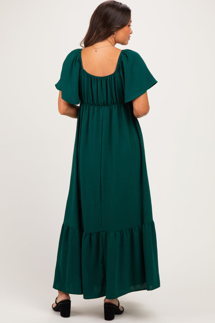 woman wearing a dark green maternity maxi dress with flutter sleeves and a tiered hem, showing a baby bump from the back