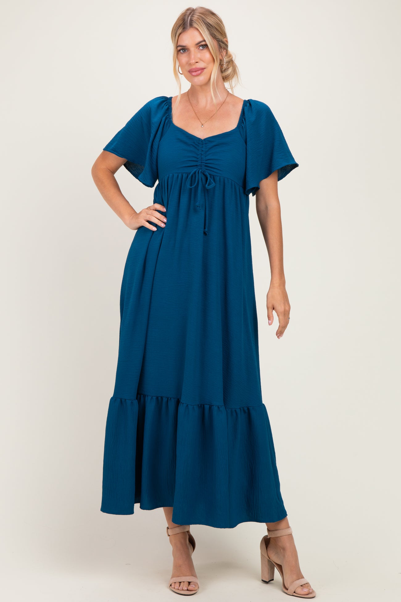 woman wearing a teal maxi dress with short sleeves, a square neckline, and a tiered skirt