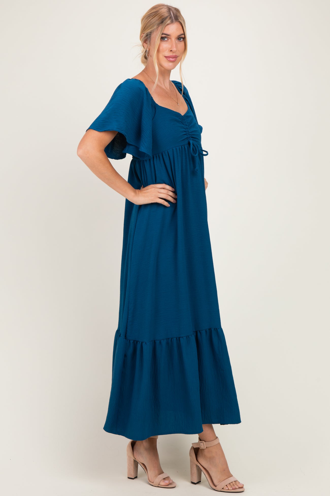 woman wearing a teal maxi dress with flutter sleeves and a tie-front detail, posing in a side view