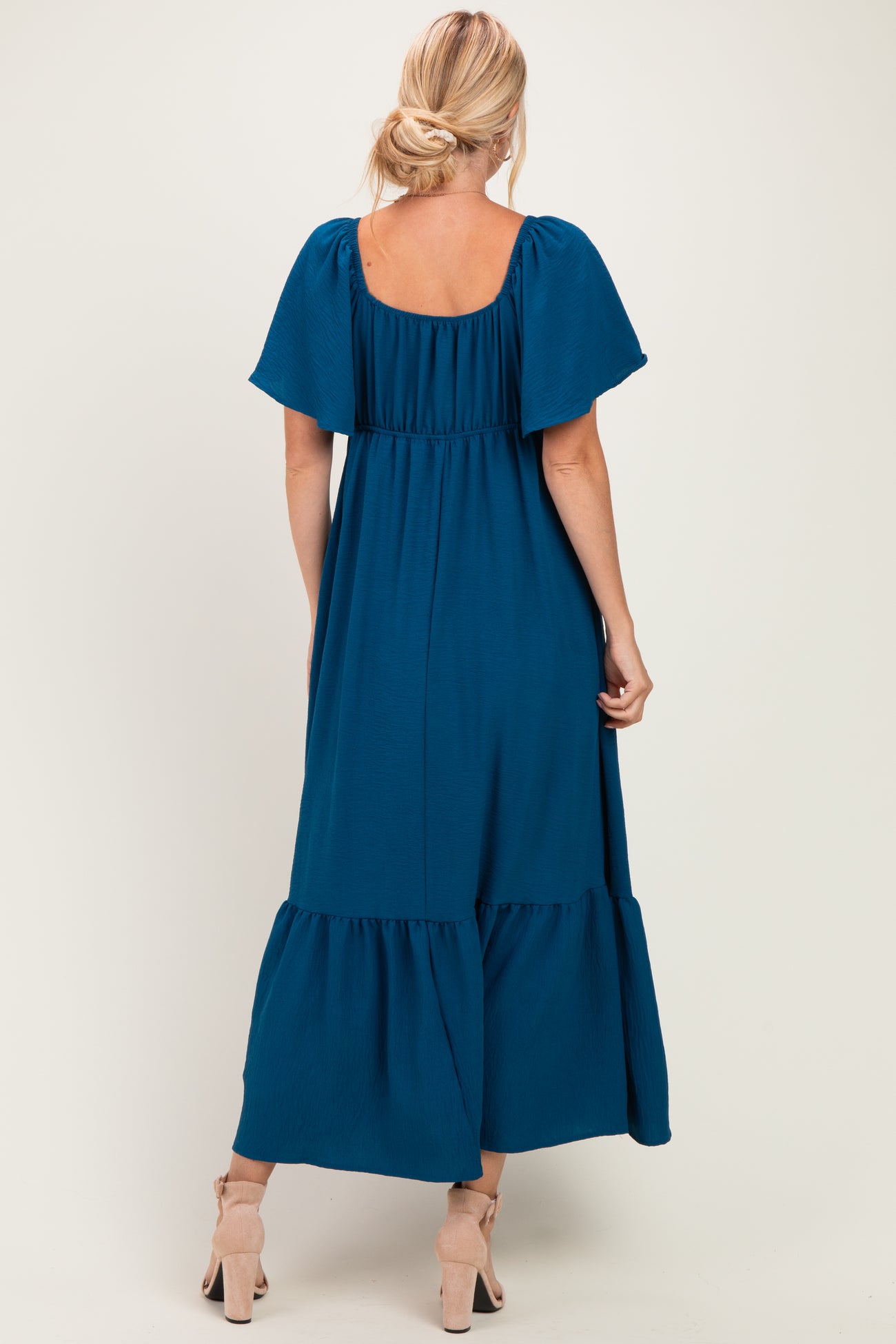 woman wearing a teal off-the-shoulder maxi dress with flutter sleeves and a tiered skirt, seen from the back