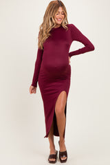 woman wearing a burgundy long sleeve maternity dress with a side slit and showing her baby bump