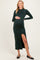 woman wearing a dark green long sleeve maternity dress with a thigh slit and holding her baby bump