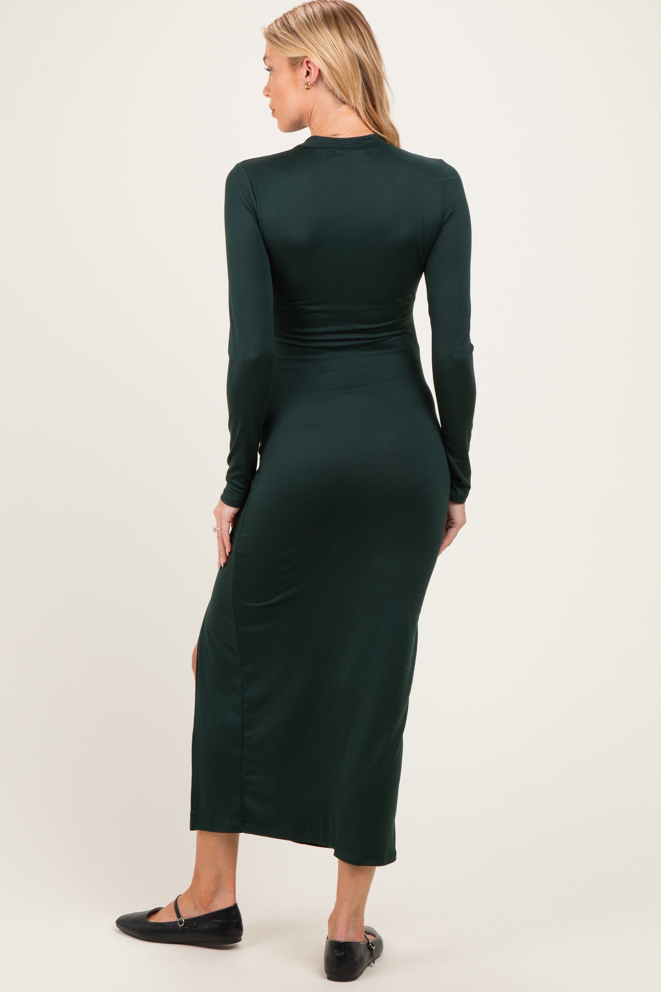 woman wearing a dark green long sleeve maternity dress with a side slit, showcasing her baby bump from the back