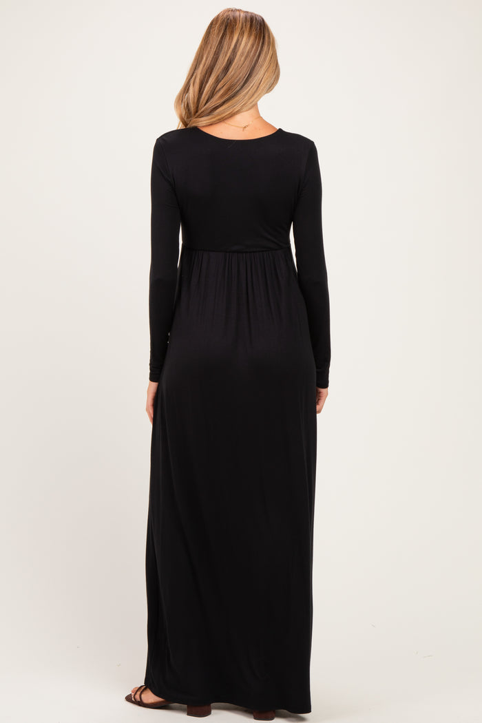 woman wearing a long black maternity maxi dress, showing the back view and fitted under the bust with a flowing skirt