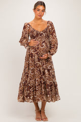 woman wearing a brown paisley print maternity dress with long sleeves, holding her baby bump