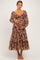 woman wearing a brown paisley print maternity dress with long sleeves, holding her baby bump