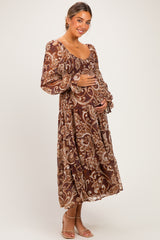 woman wearing a brown floral maternity dress with long sleeves and holding her baby bump
