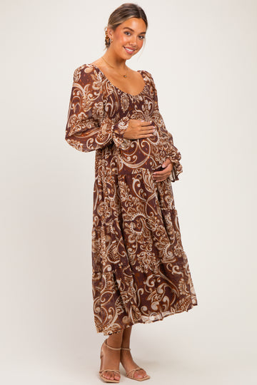 woman wearing a brown floral maternity dress with long sleeves and holding her baby bump