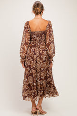 woman wearing a brown floral print maternity dress with long sleeves and a smocked back, showing a flowing silhouette