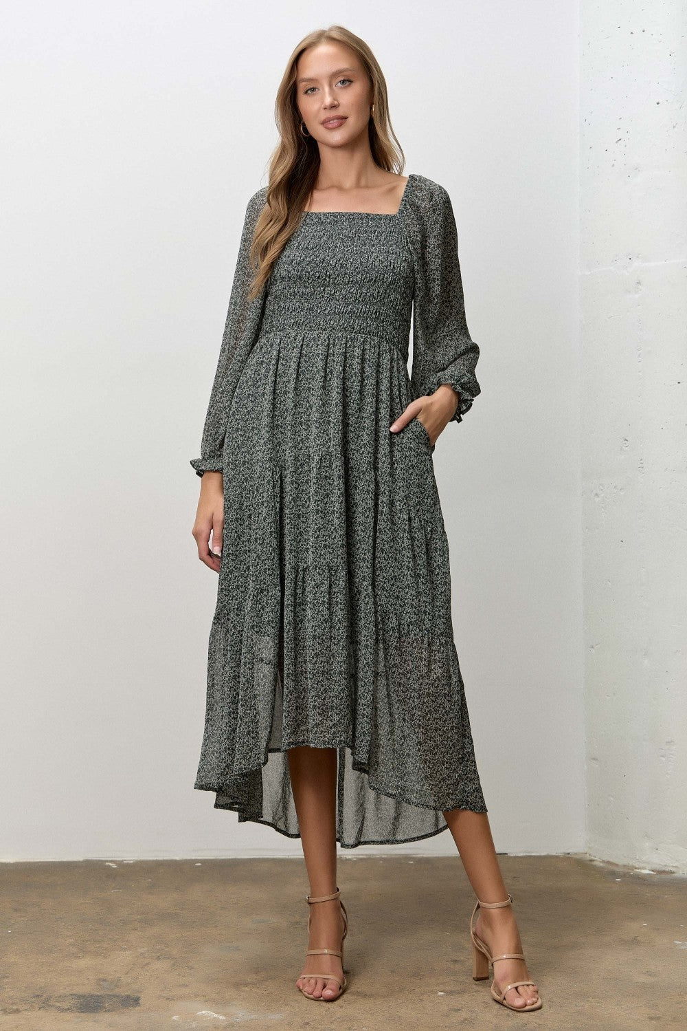 woman wearing a dark green floral mid-length dress with long sleeves and pockets, styled with strappy heels