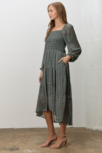 woman wearing a black and white floral midi dress with smocked bodice and long sleeves, standing in profile