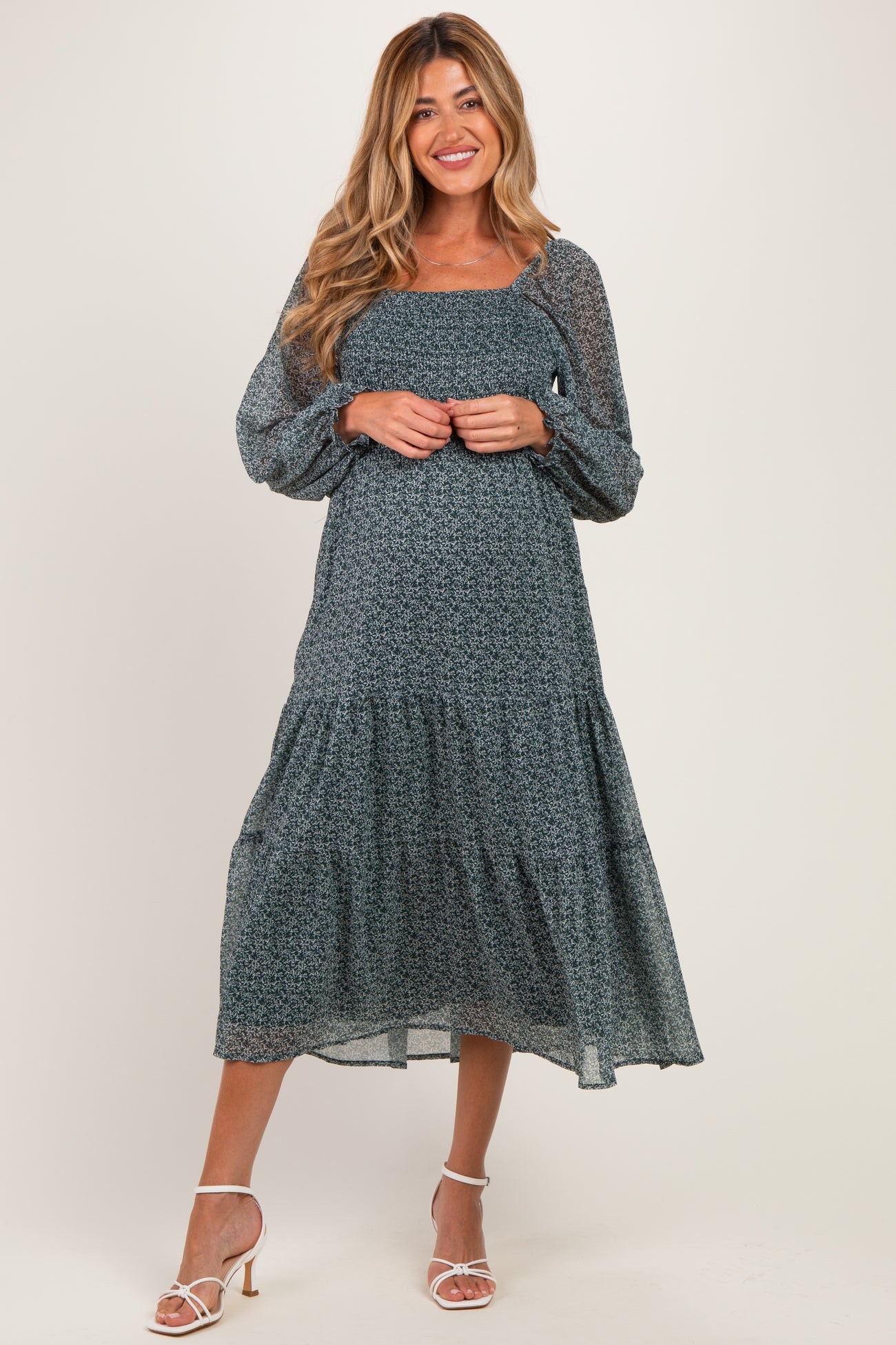 woman wearing a dark floral maternity dress with long sleeves and a tiered skirt, showing her baby bump