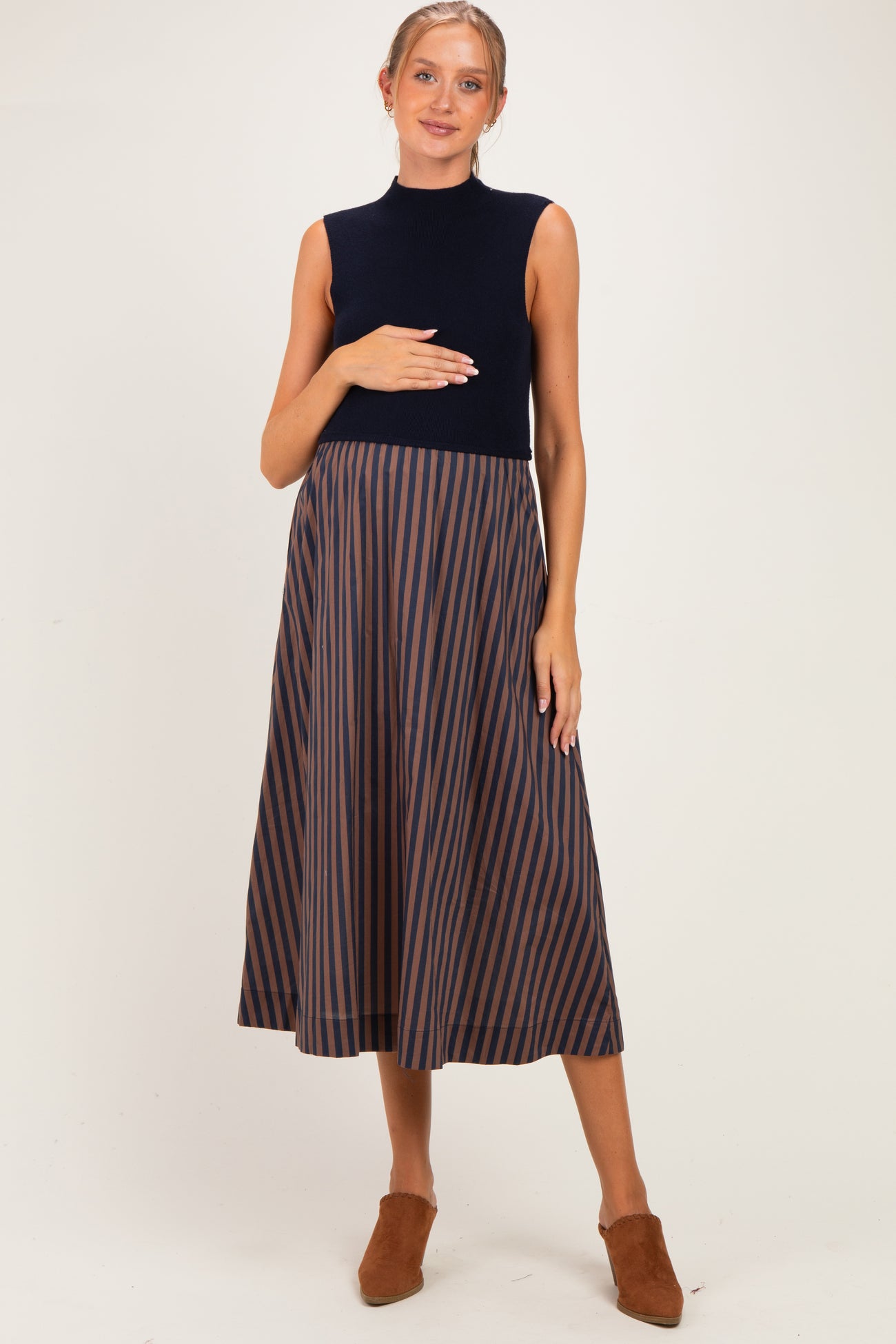 woman wearing a navy maternity dress with a sleeveless top and striped skirt, holding her baby bump