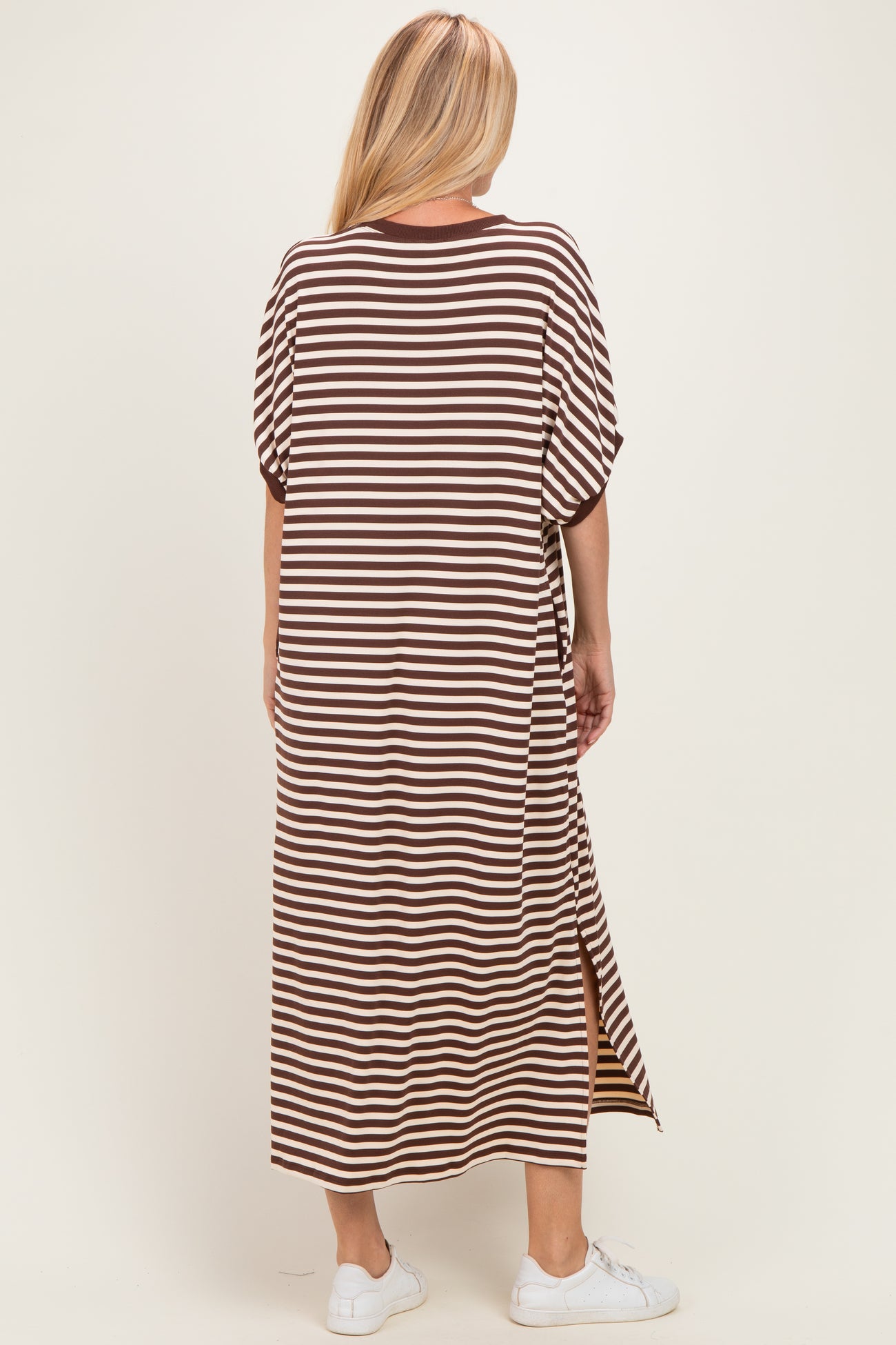 woman wearing a brown and cream striped maxi dress with short sleeves and side slits, view from the back