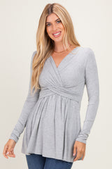 woman wearing a gray long sleeve top with a twist front and flared hem, smiling at the camera