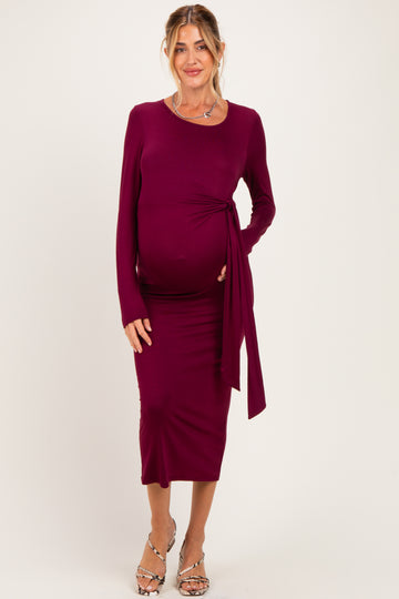 woman wearing a burgundy long sleeve maternity dress with a side tie detail and holding her baby bump