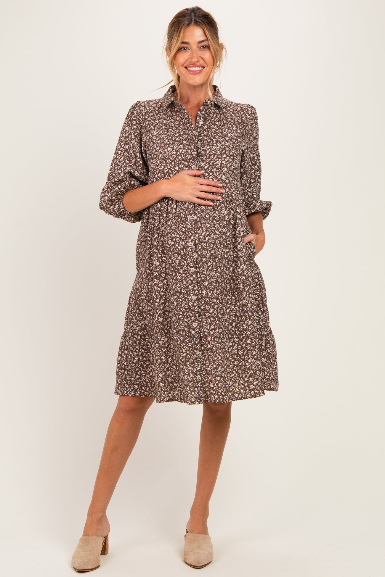 woman wearing a brown floral maternity dress with buttons and pockets, showcasing her baby bump